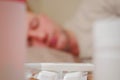 White thermometer on a pack of pills and two bottles with medicine in focus, sick man sleeping in bad out of focus in the Royalty Free Stock Photo