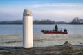 White thermos on fallen tree on blurred background of fishing boat at river Royalty Free Stock Photo
