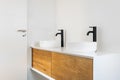 White tiled bathroom with two wash basins, black faucets and wooden cabinets. Royalty Free Stock Photo