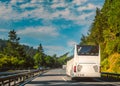 White tour bus or coach on a two lane motorway travelling through a tree lined hilly countryside on a sunny day