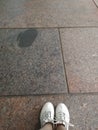 White tourist sneakers are on the brown marble floor. The floor is gray and brown squares. Tourist pending.