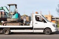 A white tow truck transports a green small tractor to the platform. Construction machinery transfer. Motion blur. Riga, Latvia -
