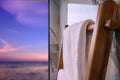 White towel hanging on a minimal wooden ladder, blurred sunset beach in background. modern bathroom Royalty Free Stock Photo