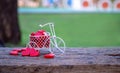 White toy bike carrying red wood hearts. Red wood hearts fall on the wooden floor, green background of grass. Heart-shaped toys Royalty Free Stock Photo