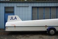 White trailer for a sailplane in front of a blue industrial building