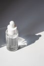 A white transparent bottle with serum in the rays of the sun.