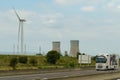A white truck drives down the highway next to a huge wind turbine.