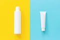 White tube and bottle of sunscreen or other cosmetic product on yellow and blue paper background. Mock up Template for lettering,