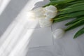 White tulip flowers bouquet and blank paper card mockup on neutral marble table with abstract natural sunlight shadows Royalty Free Stock Photo