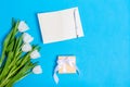 White tulips bouquet with gift box  greeting card and pen on light blue background Royalty Free Stock Photo