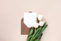 White tulips, envelope with blank sheet on neutral beige background. Valentine's Day, Mother's Day holiday