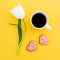 White tulips flowers with mug of coffee and cookies on yellow background. Love composition. Flat lay, top view. Royalty Free Stock Photo