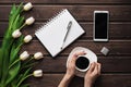 White tulips on a wooden table with an empty notebook and smartphone and a Cup of coffee in women`s hands Royalty Free Stock Photo