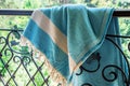 A white and turquoise Turkish peshtemal / towel on a wrought iron railings with blurry nature in the background. Royalty Free Stock Photo