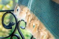 A white and turquoise Turkish peshtemal / towel on a wrought iron railings with blurry nature in the background.