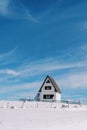 White two-story house with a triangular roof with a wooden fence on a snowy hill