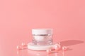 White unbranded cosmetic cream jar standing on white podium. Skin care product presentation on the pink background with