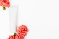 White unbranded cosmetics tube with roses. Cosmetology container for facial or hand cream, moisturizing lotion on light backdrop.
