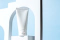White unbranded plastic squeeze tube for cream or shampoo stands on white podium in white arch on blue background