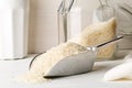 White uncooked, raw long grain rice in metal scoop with glass storage jar on white kitchen table background