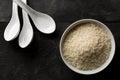 White uncooked, raw long grain rice in white bowl with spoons on black wooden table top view flat lay from above Royalty Free Stock Photo