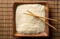 White uncooked, raw long grain rice on wooden plate with chopsticks on bamboo mat with copy space top view flat lay from above Royalty Free Stock Photo