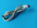 White USB type C charging cable, compatible for many devices, tied in a ribbon shape, isolated on a blue background. Royalty Free Stock Photo