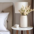 White vase with flowers on round nightstand near bed. Art deco style interior design of modern bedroom Royalty Free Stock Photo