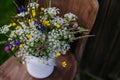 White vase with meadow flowers, herbs and grass, placed on a wooden chair. A colorful variety of summer wildflowers. Royalty Free Stock Photo