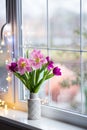 White vase with tender bouquet of beautiful pink tulips near window with raindrops in the daylight