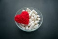 White veg capsules and red thread heart in glass bowl on black b