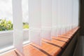 White vertical window blinds slats with cordless glued weighted pockets on the end casting shadows on the wooden window sill