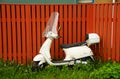 A white Vespa motor scooter at a brown fence