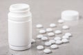 A white vial and a handful of white tablets or vitamins or nutritional supplements on a marble table