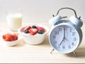 White vintage alarm clock 7 am. with breakfast set, oat or granola in white bowl, fresh blueberries and strawberries, a  glass of Royalty Free Stock Photo