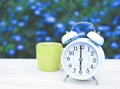 white vintage alarm clock and green cup of coffee on the table in the garden with purple flowers background Royalty Free Stock Photo