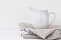 White vintage pitcher on a stack of linen towels, styled image with copyspace for product marketing