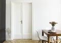 A white wall with double door next to a wooden breakfast table and chairs in a dining room interior. Real photo. Royalty Free Stock Photo