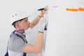 In the white wall, holes are made and orange dowels are hammered with a hammer, a worker in a protective helmet Royalty Free Stock Photo