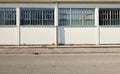 White wall with large windows. Concrete sidewalk and asphalt road in front.