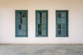 White wall with three green grunge wooden window shutters, wrought iron bars and marble floor