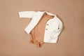 White warm knitted sweater with white, brown bodysuits on beige background. Collection of cute baby clothes for cold weather Royalty Free Stock Photo