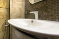 White washbasin with a modern ball valve against a brown mosaic and natural yellow stone tiles