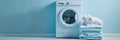 A white washing machine sits against a light blue wall, with a neatly folded stack of clean laundry beside it Royalty Free Stock Photo