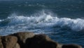 White wave on ocean surface, on a blustery, windy day with rocks in foreground.