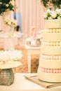 WHITE  WEDDING CAKE AT IMPRESSIVE COLOURFUL VENUE WITH BEAUTIFUL CANDY TABLES, FLORAL GREEN DECORATION, BLURRED BACKGROUND, YELLOW Royalty Free Stock Photo