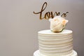 a white wedding cake with a white rose on top with the word love written above Royalty Free Stock Photo