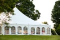 A white wedding tent set up in a lawn surrounded by trees and with the sides down