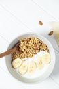 white wheat and granola with low-fat yogurt in a white bowl in a composition with a spoon, honeycombs, banana on white wooden
