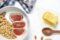 white wheat granola with low-fat yogurt in a white bowl in a composition with a spoon, honeycombs and fig on white wooden